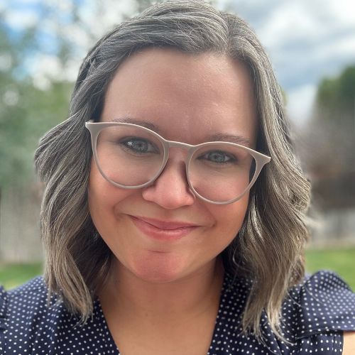 Olivia Earle smiling in a blue blouse with white polka dots, standing outside