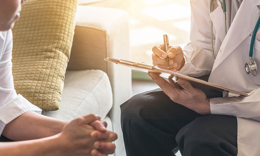 A patient sitting on a sofa is being asked survey questions by his doctor.