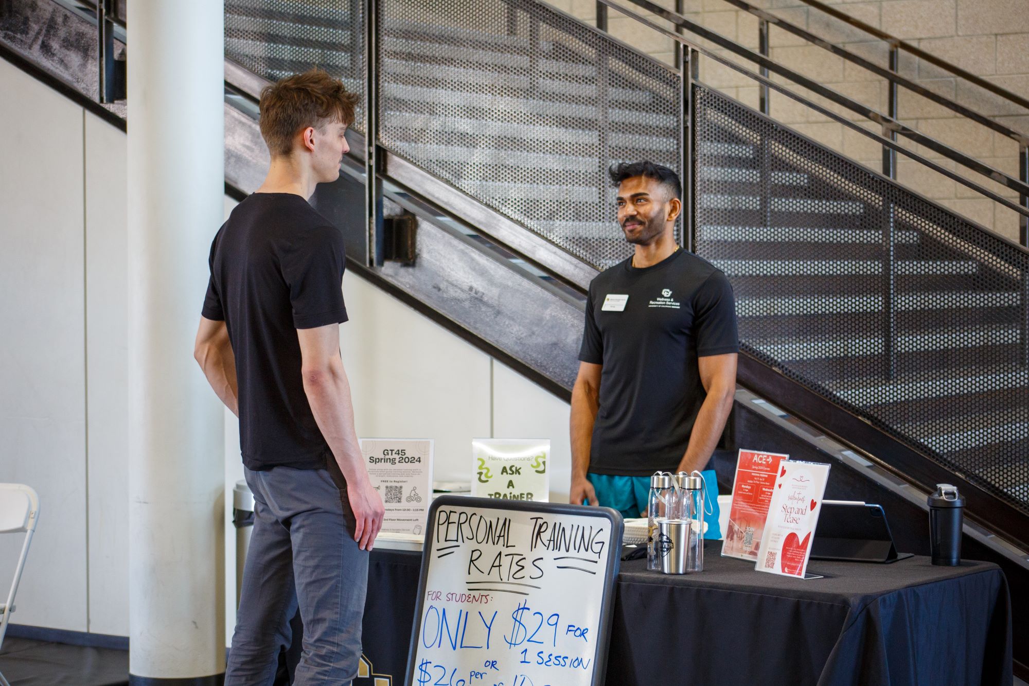 a personal trainer standing behind a table talking to a man