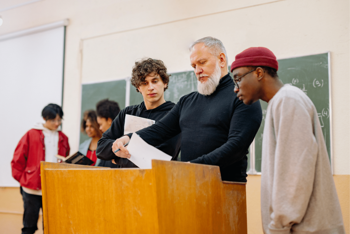 Two students getting help from their professor while a group of other students are standing in the background.
