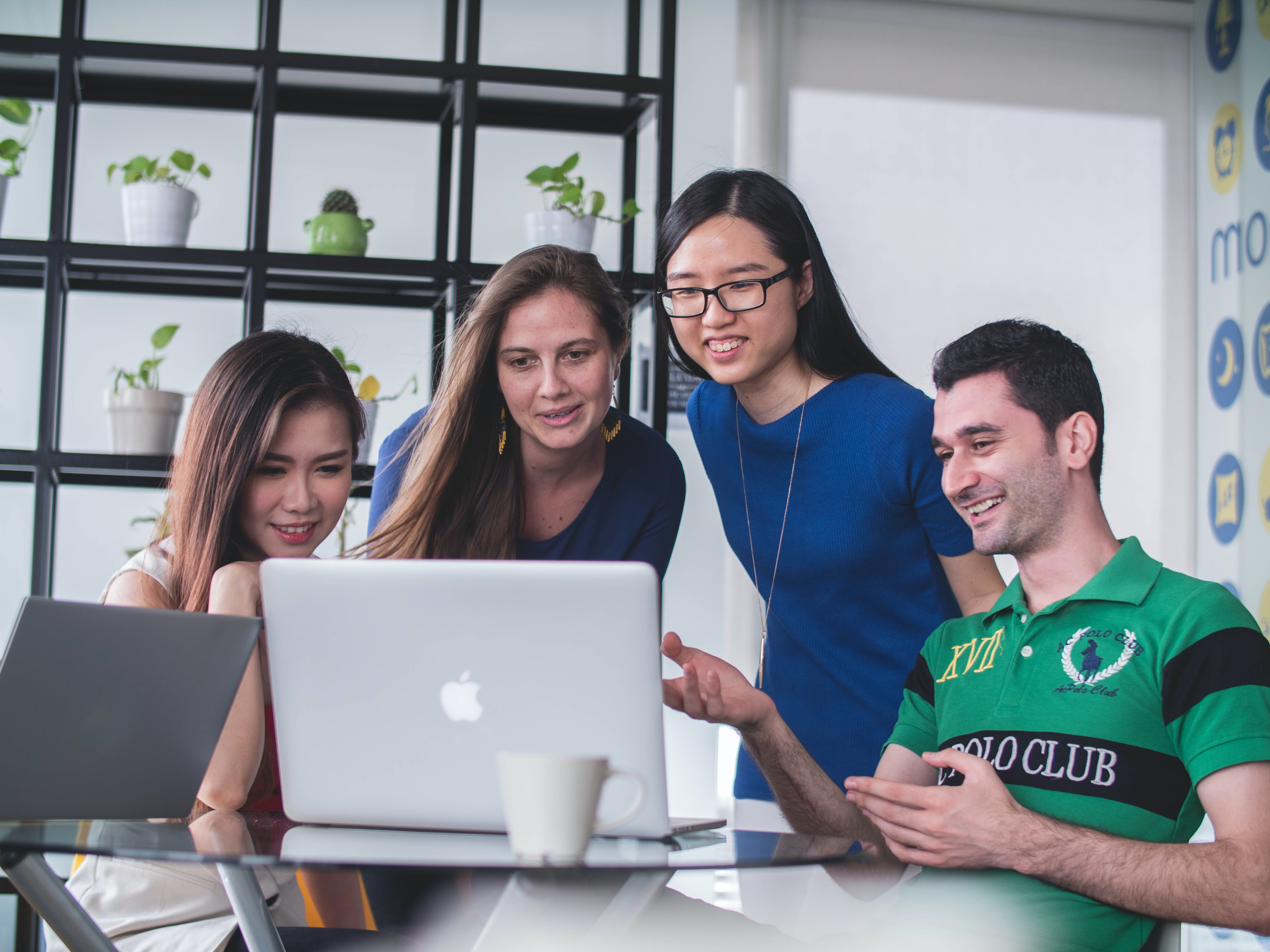 A woman and three young people all smile while looking at a laptop screen.