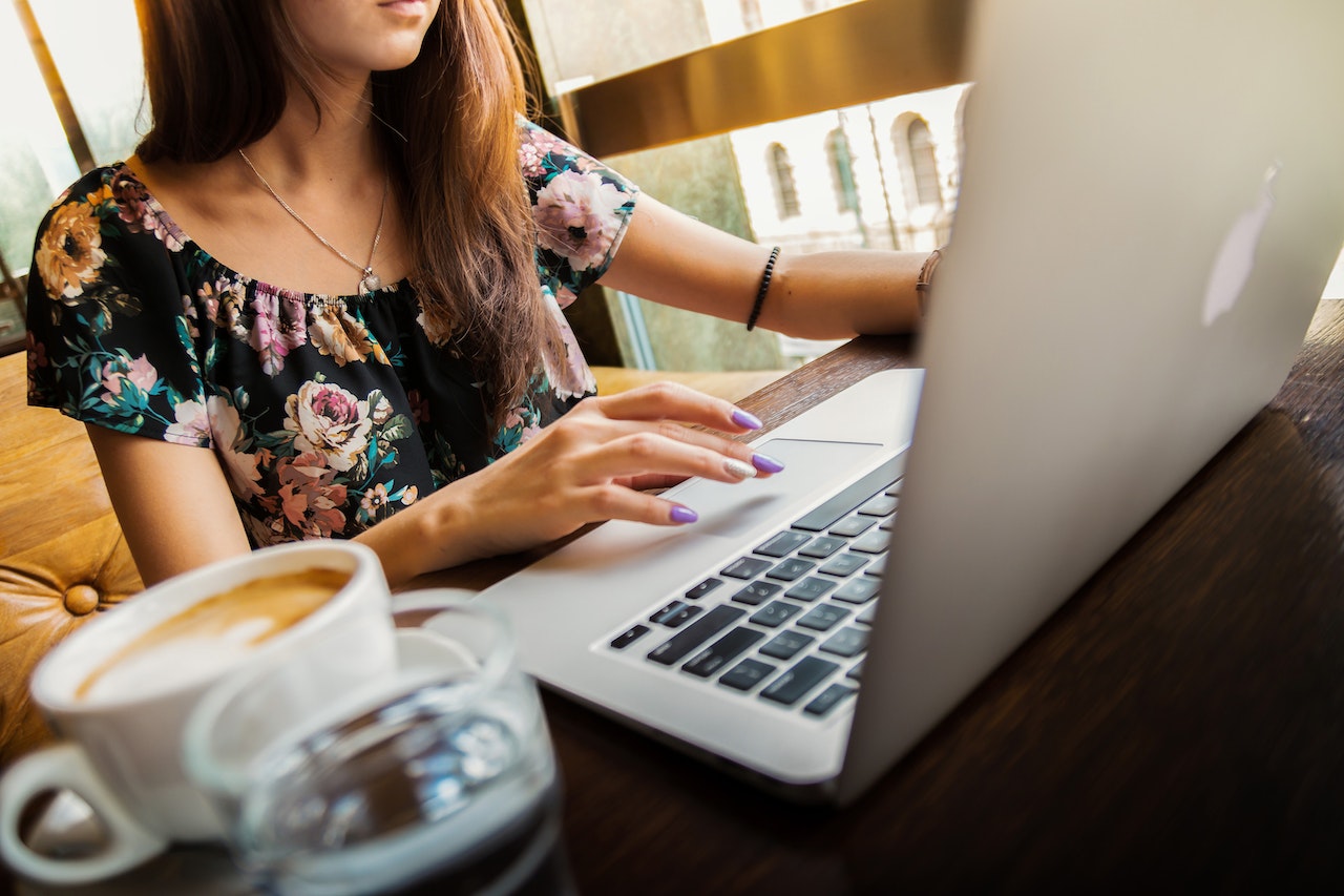 A close-up of a woman working on a laptop with a coffee mug and glass of water beside her.