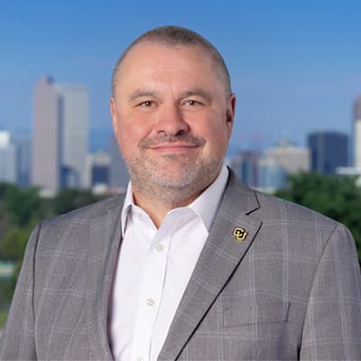 Man in a gray suit jacket and white button up with a closed-mouth smile.