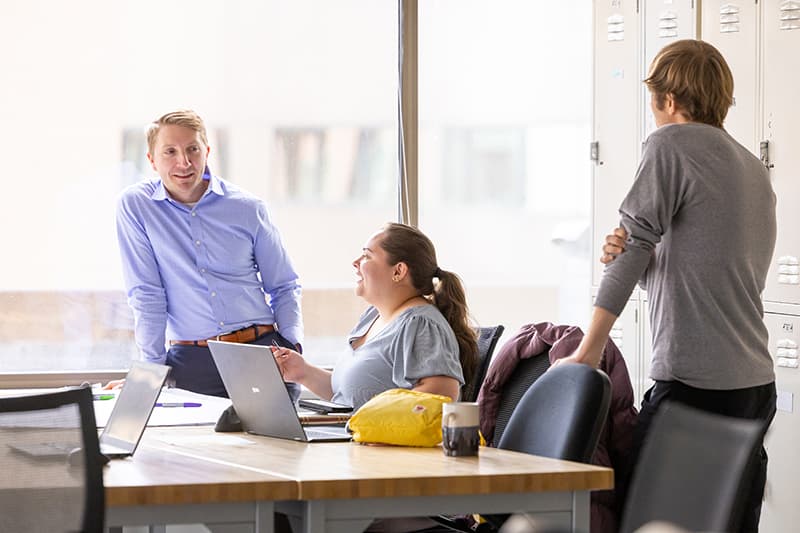 Three people are gathered around a table smiling and working together.