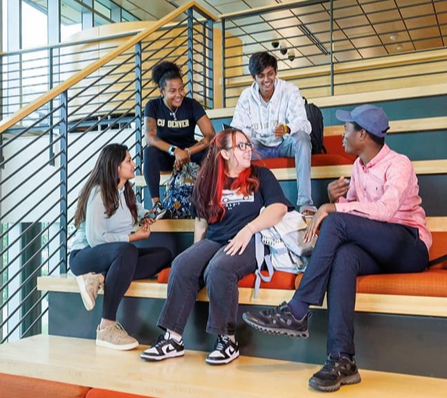 Five students seated on stairs interacting with each other.