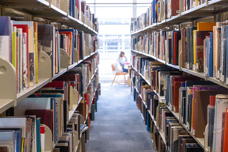 Aisle of a library with shelves of books on either side.