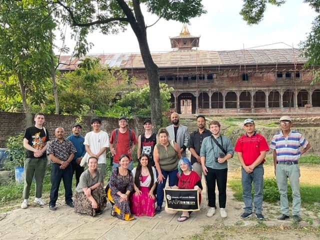 16 people grouped together smiling and holding a CU Denver banner outside in Nepal..
