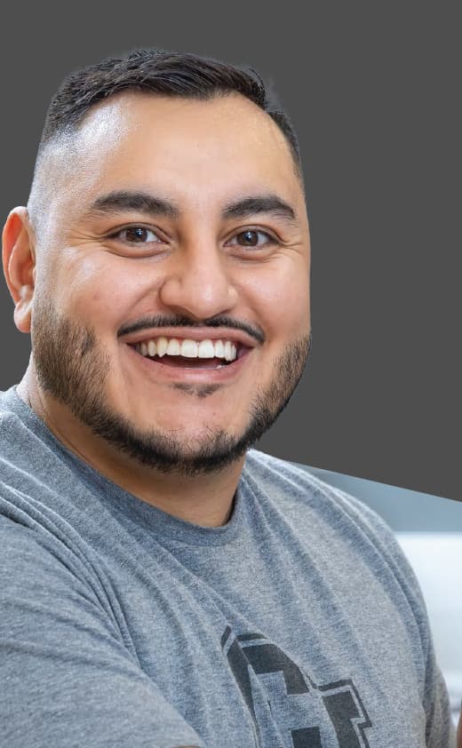 Man in a gray t-shirt and facial hair smiling with his teeth.