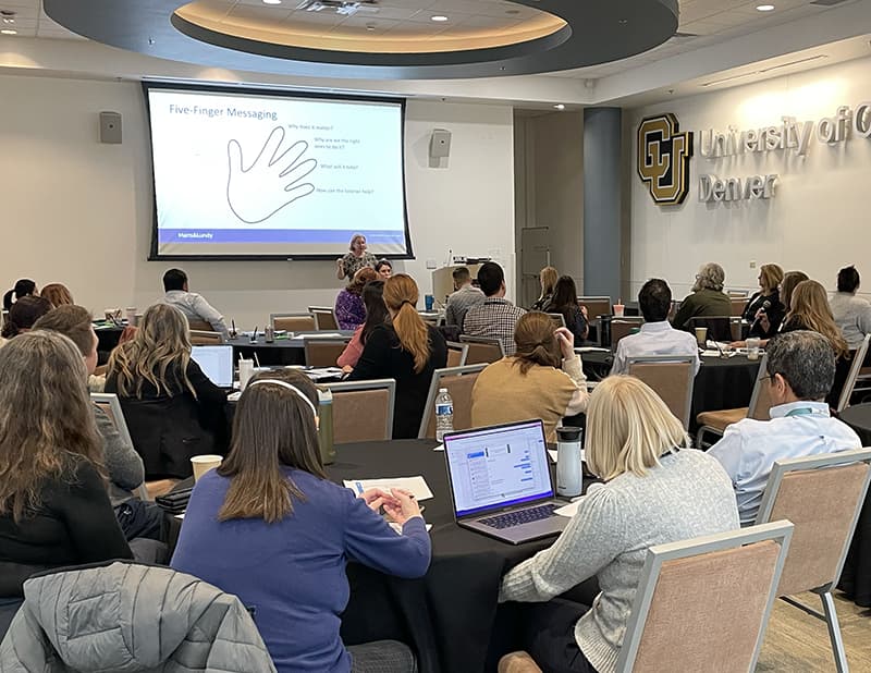 Room full of people watching a presenter who has a slide up featuring a hand.