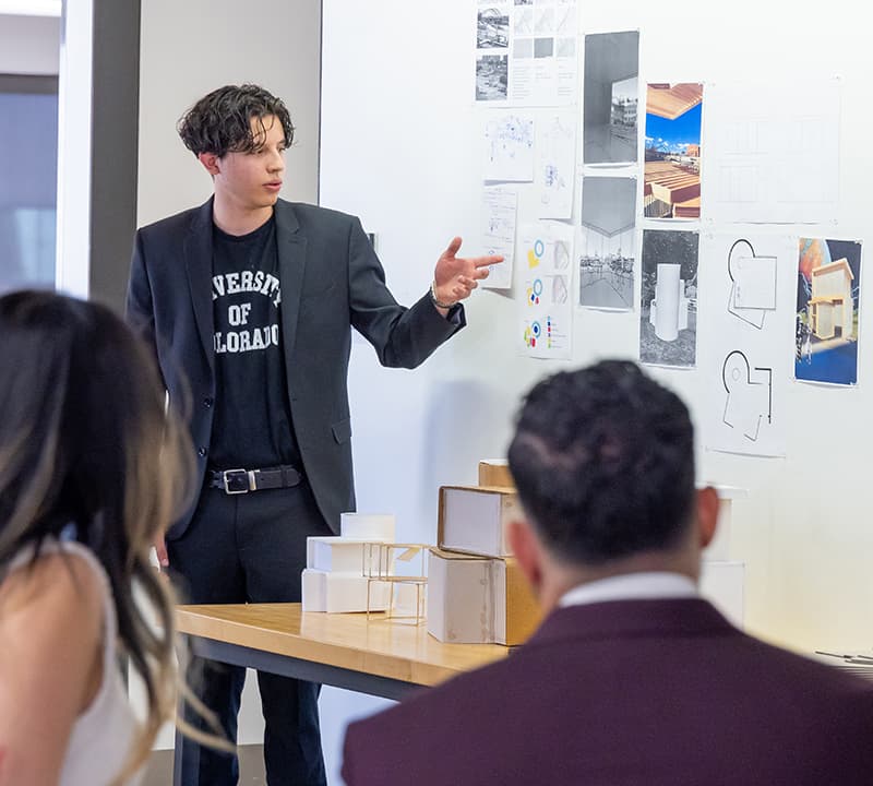 Student presenting renderings to a group in a classroom.