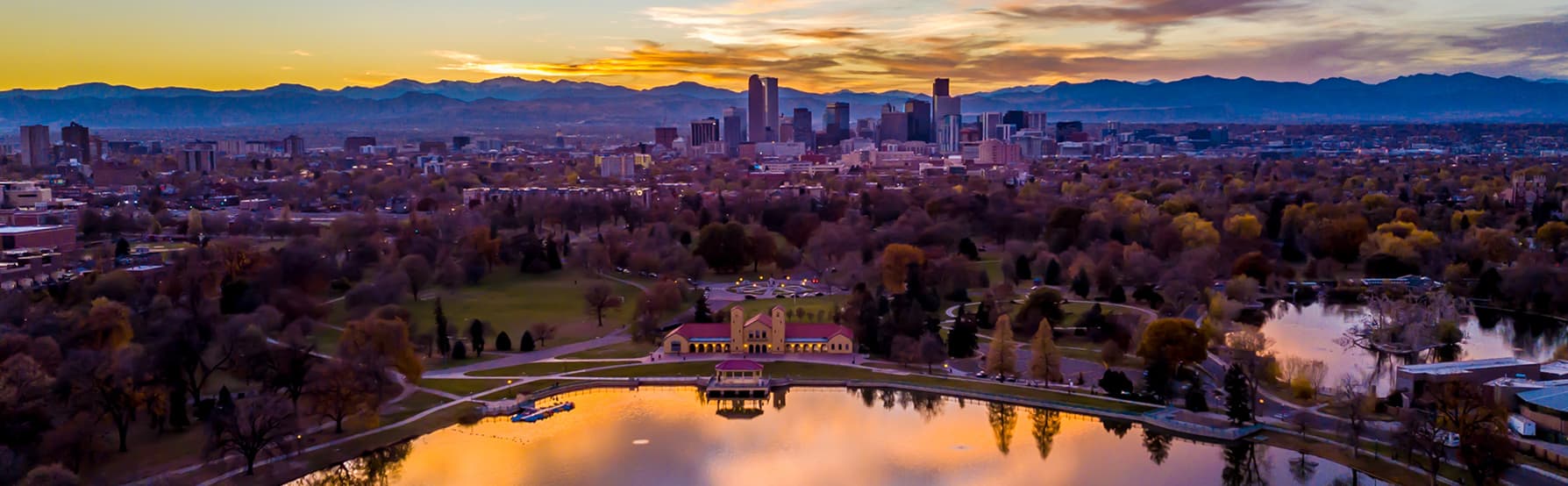 Aerial view of Denver skyline against gold clouds with City Park in the foreground.