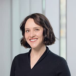 Woman in a dark blouse and short hair smiling with her teeth.