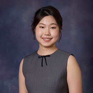 Woman in a gray sleeveless dress and dark hair that's pulled back, smiling at the camera.