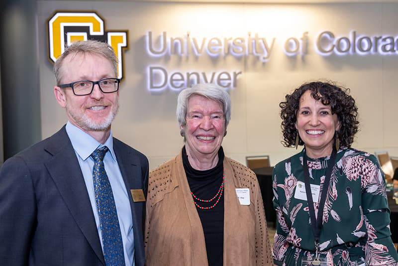 Three people in business attire stand together smiling.