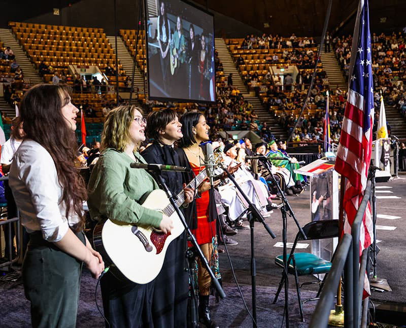 Four people singing on stage at commencement.