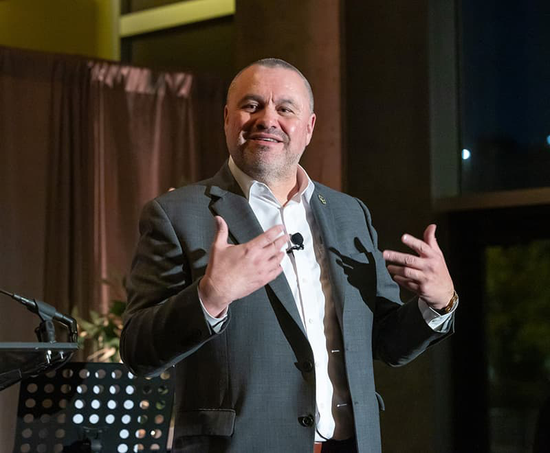 A man in a suit speaking to a crowd mid-hand gesture. 