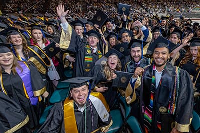 Large group of graduates in commencement regalia cheering in celebration.
