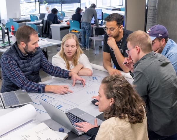 Students gather around a faculty member who is explaining a concept on paper