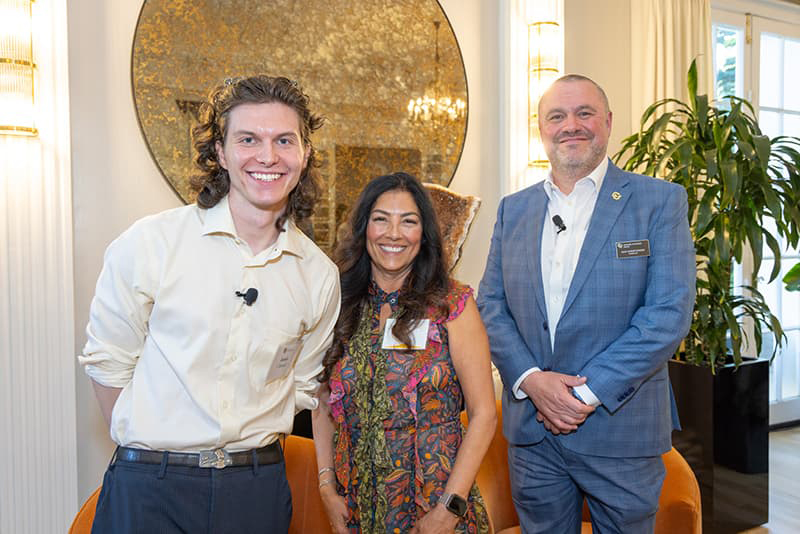 Three people in business professional attire stand together and smile proudly. 