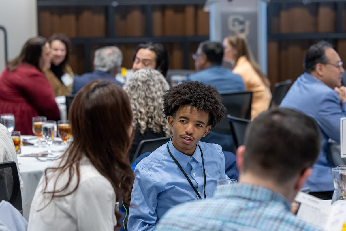 Several round tables with students in business attire engaging with one another.