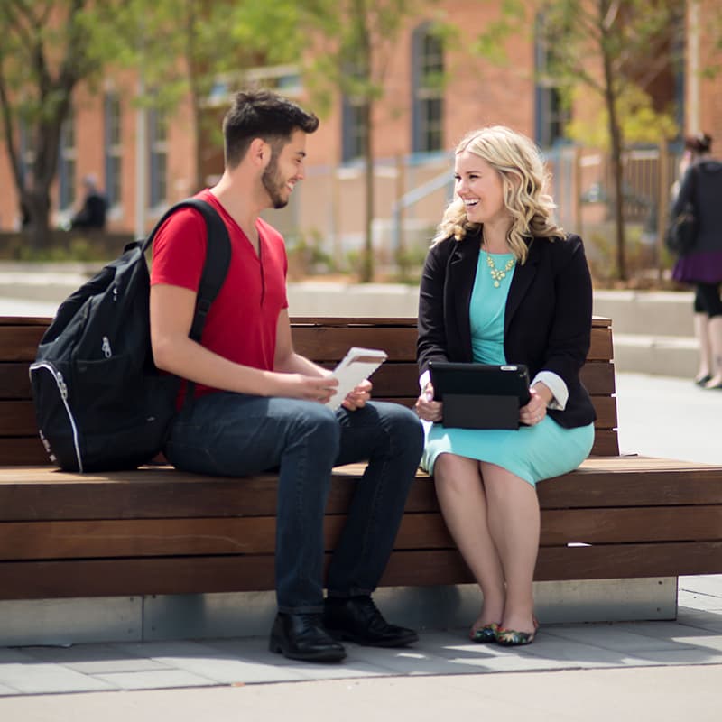 Two people seated outside engaging with each other and smiling.