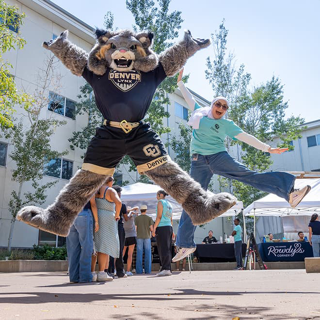 Milo the Lynx mascot jumping in the air with a student with arms and legs out.