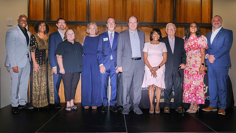 Group of 11 people in professional business attire smiling proudly.