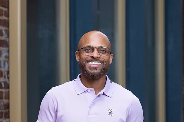 A man in a pink polo and glasses smiling with his teeth.