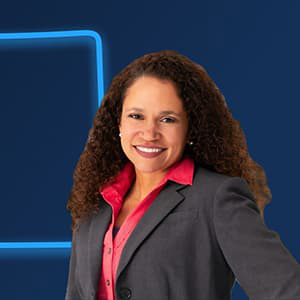Brandy Reitter in a gray suit and pink blouse with long, dark curly hair, smiling with her teeth.