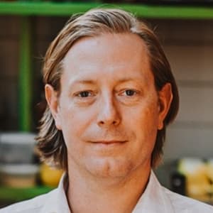 Man with hair at his jaw-line in a collared shirt and closed mouth smile.