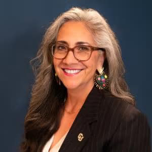 Woman with classes and a black blazer smiles with her teeth.