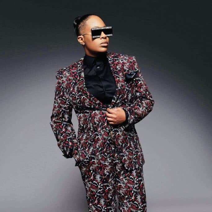 Erin Hall in a bold red and gray patterned suit with large, dark, square sunglasses, very editorial.