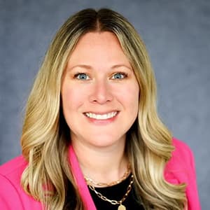 Woman with long blonde hair and a bright pink blazer smiles with her teeth.