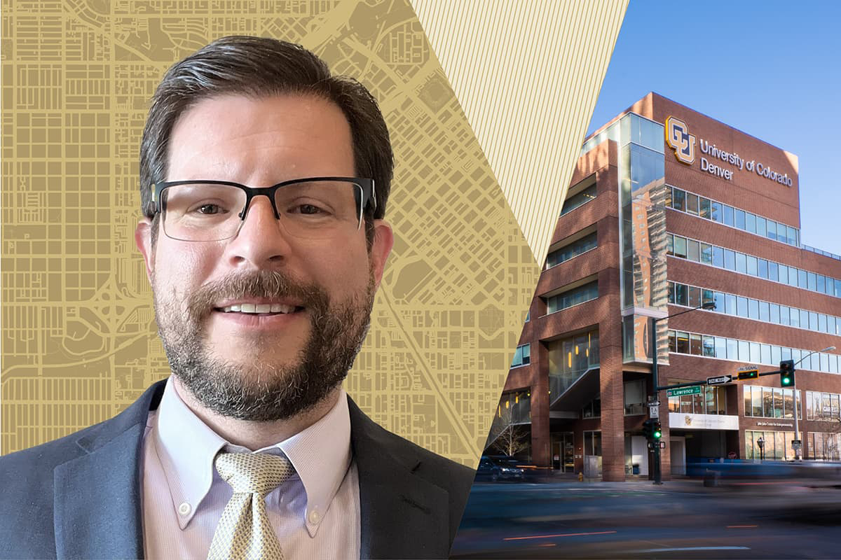 John Bailey in a suite, tie, and glasses smiling with his teeth on a CU Denver stylized banner.