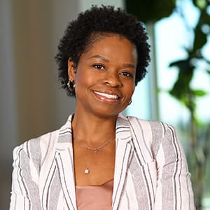 Woman in a plaid suit jacket and short black hair smiles with her teeth.