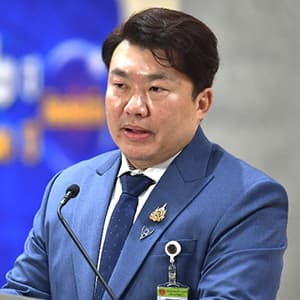 Man in a blue suite with dark hair speaks at a microphone.