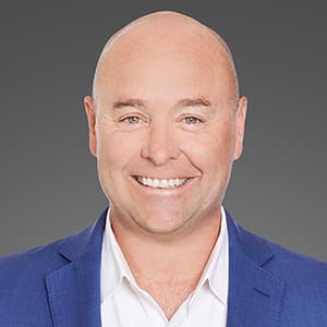 Bald man smiling with his teeth wearing a blue suit jacket and white shirt.