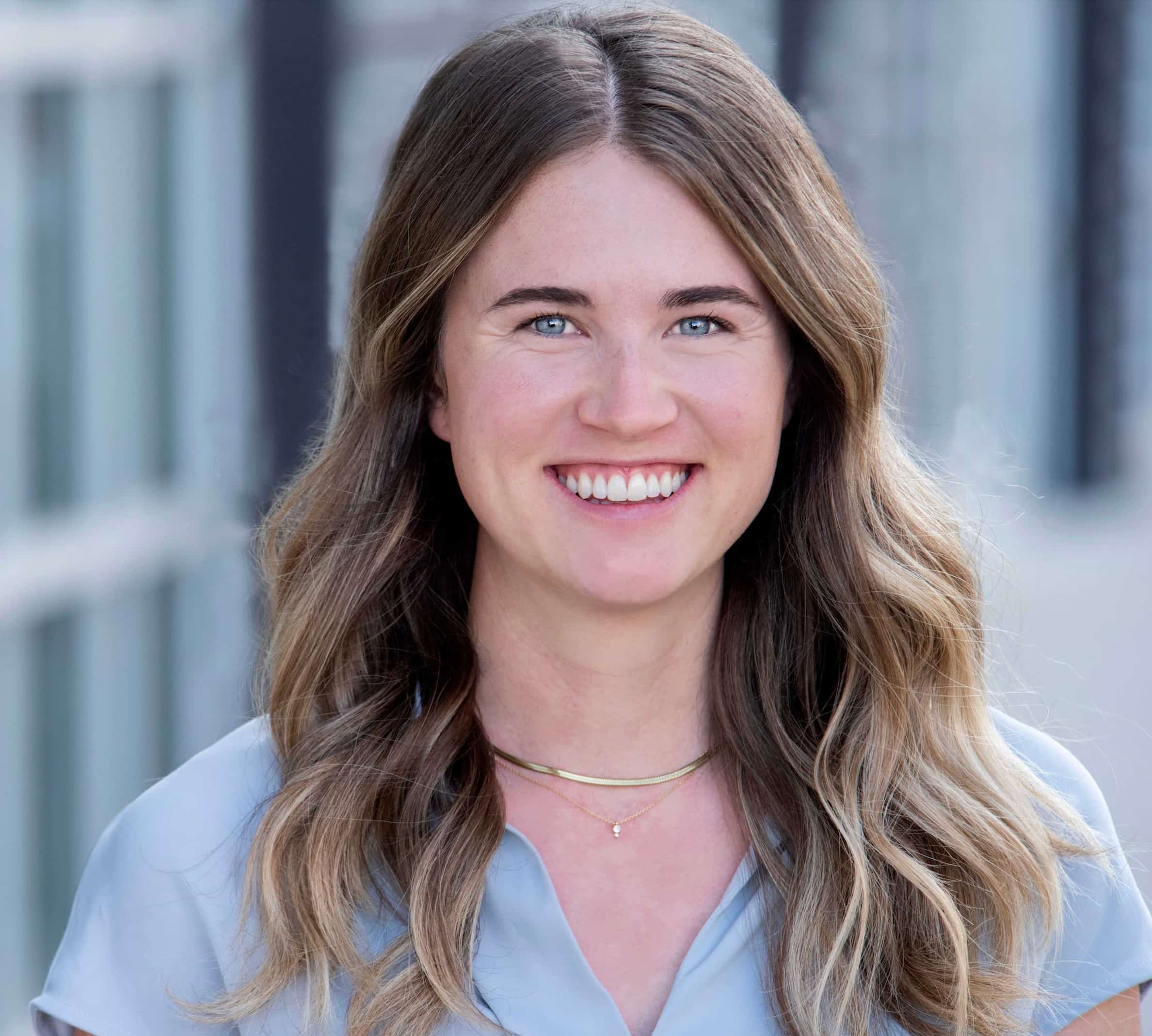 Claire, a caucasian woman with long brown hair, stands in front of a grey background.