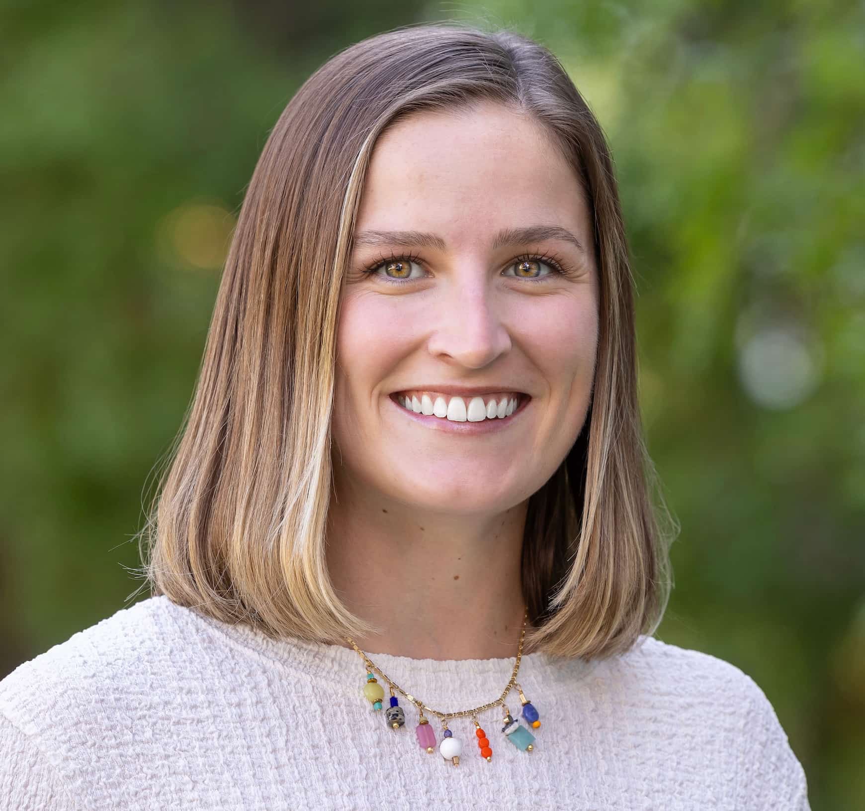 Jackie, a caucasian woman with brown hair, stands in front of a tree.
