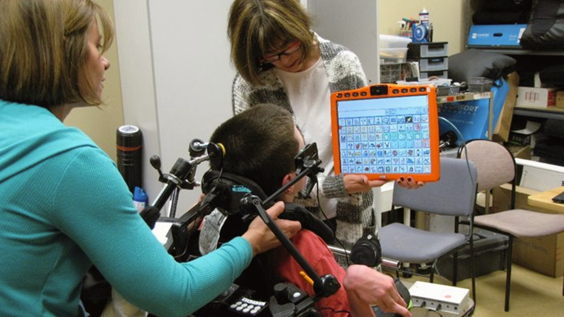Clinicians support young boy in a wheelchair with Alternative Augmentative Communication (AAC)
