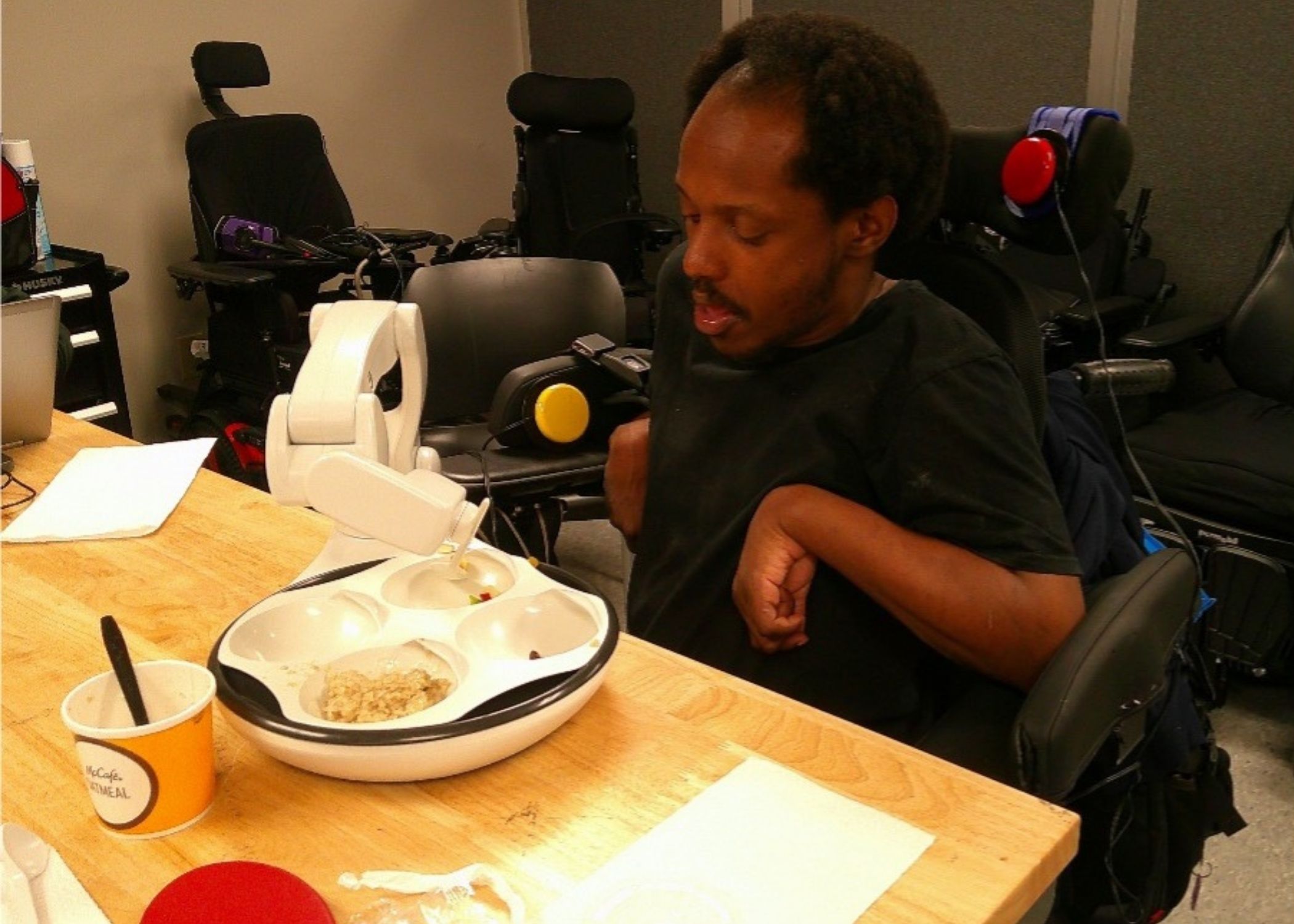 Tim sits at a table using the Obi assistive eating device
