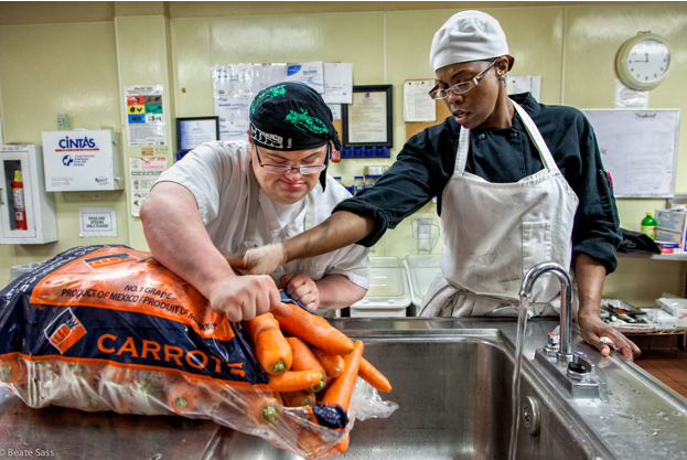A person with downs syndrome cleans carrots at a sink