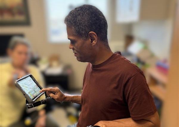A person uses a small AAC device mounted on their walker.
