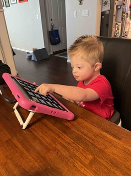 aacdevice a child sitting at a table and tapping on an aac device