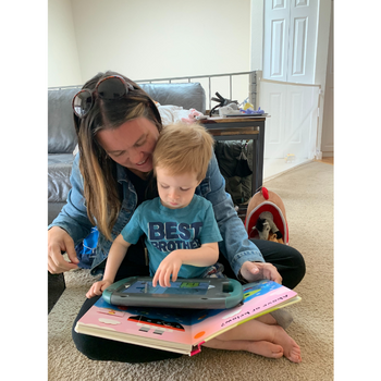 ipadaac a child using an aac device on top of a large book while sitting in a womans lap